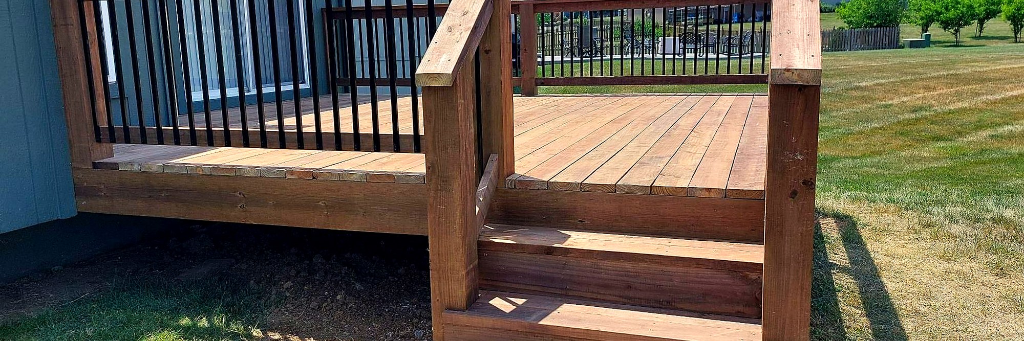 Stained deck with a black metal railing on a bright day.