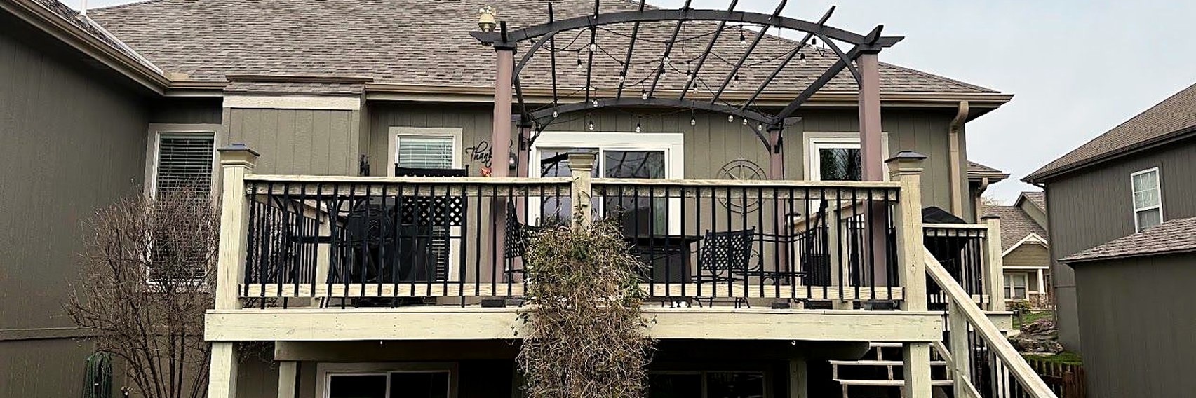 Deck with a pergola on the back of a grey two-story home.