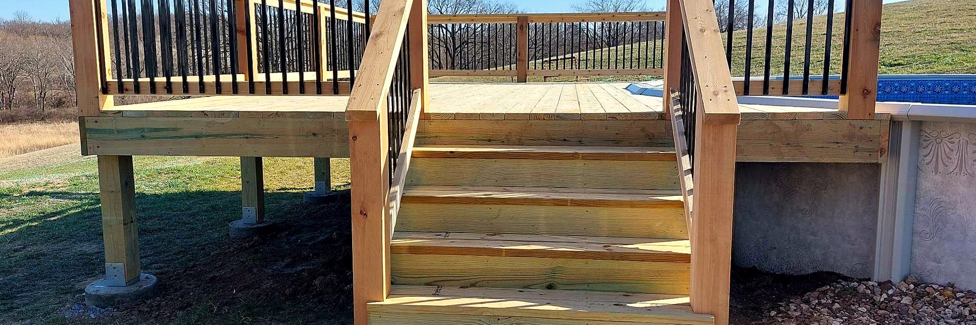 Deck with black balusters and a wide stair run down to a concrete pad.