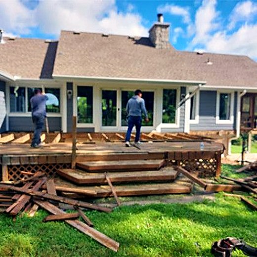 Crew tearing out an old wooden deck, boards stacked on the lawn.